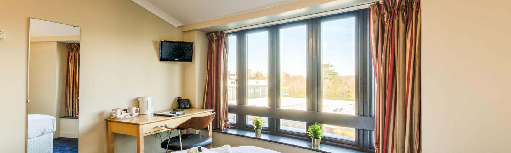 Photo of a hotel room with double bed, mirror, desk, TV and large windows
