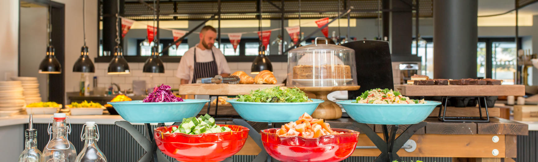 Photo of a cafe with salad bar in the foreground, and cakes, pastries and hot food in the background