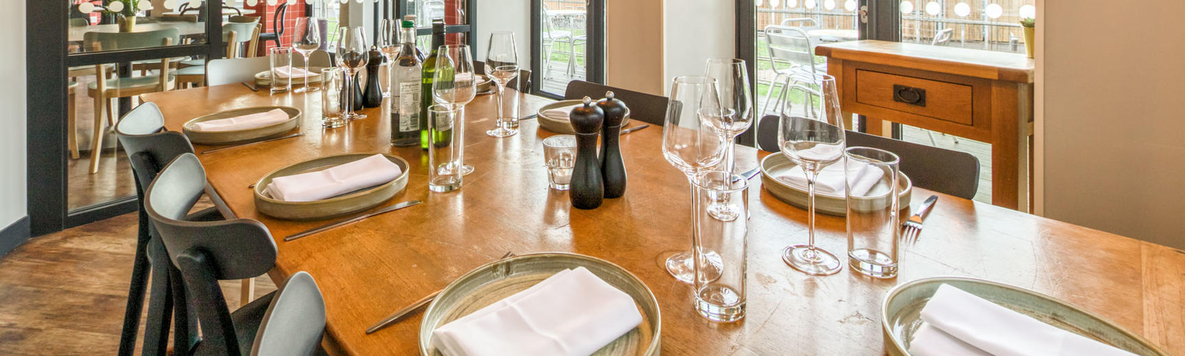 Photo of a large dining table set for dinner with crockery, cutlery and glasses and surrounded by large windows looking out into the cafe area