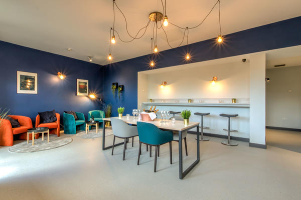 Photo of a bar seating area with dark blue walls, a striking modern light fitting, and various chairs and tables around the room