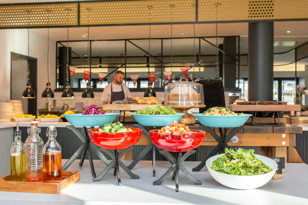 Photo of a cafe with salad bar in the foreground, and cakes, pastries and hot food in the background
