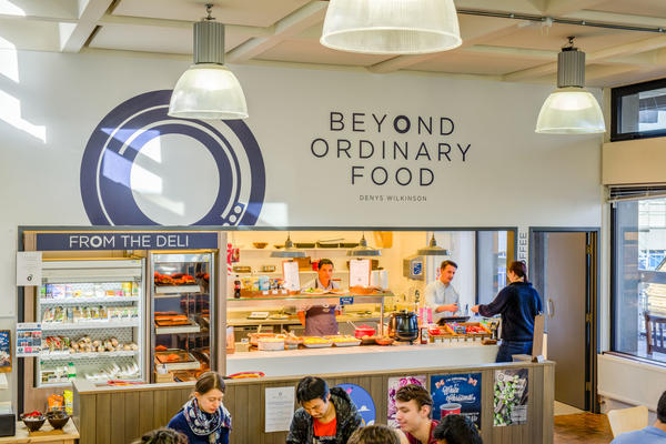 Photo of a cafe with 'Beyond Ordinary Food' text and logo on a white wall above the serving hatch
