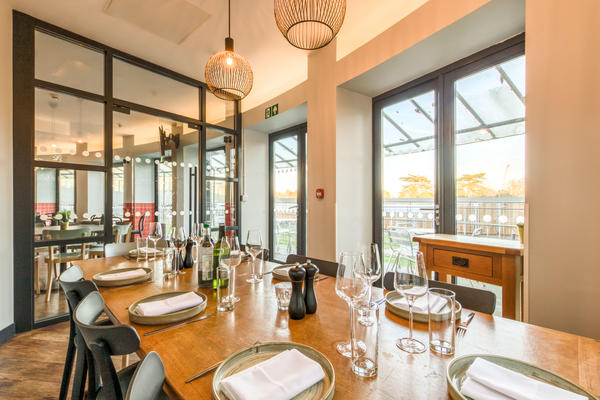 Photo of a large dining table set for dinner with crockery, cutlery and glasses and surrounded by large windows looking out into the cafe area