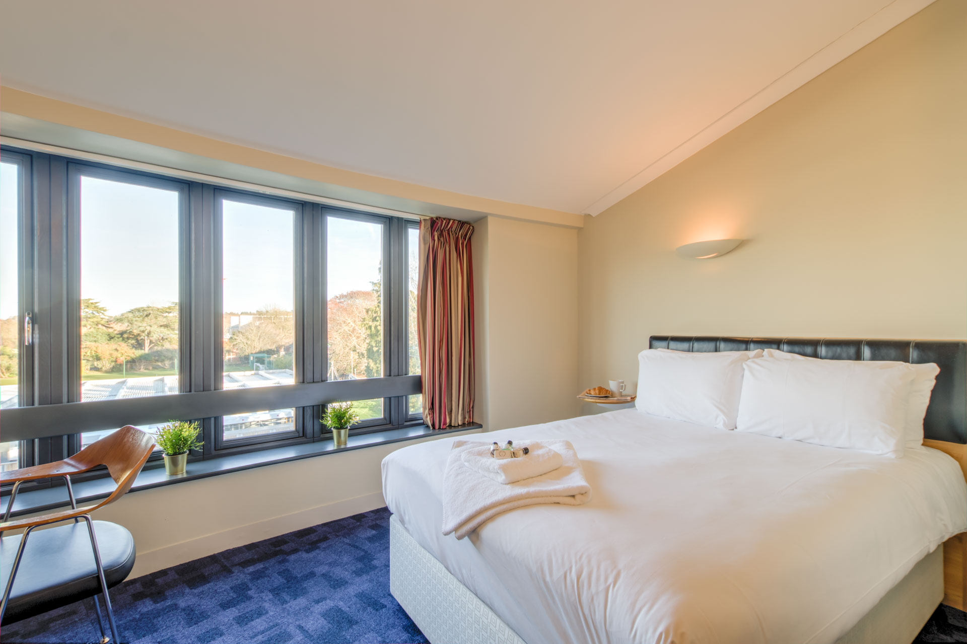 Photo of a hotel room with large double bed, desk, chair and large windows